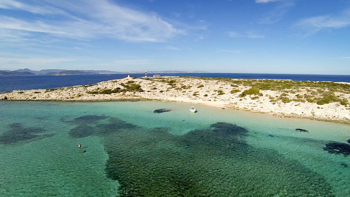 The image shows a landscape of Ibiza and an island called Espalmador, with clear blue waters and white sand, that you can visit with our boats for rent